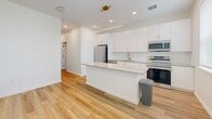 Located at 14520 Avalon Rd in Winter Garden, FL, this single-story, one-bedroom, one-bathroom unit offers a thoughtfully designed layout that maximizes functionality. Light wood-style flooring flows throughout the space, complemented by crisp white walls and recessed lighting that create a clean, modern aesthetic.

The heart of the unit is a combined living, dining, and kitchen area. The kitchen stands out with sleek white cabinetry, granite countertops, a white subway tile backsplash, and a full suite of stainless steel appliances including a French door refrigerator, electric range, and over-the-range microwave. A central island with matching granite provides additional prep space and seating, while a linear pendant light and ceiling fan add stylish overhead illumination. Natural light enters through a window overlooking the space.

A hallway fitted with a sliding barn door connects the main living area to the private spaces. The bedroom is a cozy, well-proportioned room with recessed lighting and a ceiling fan. A dedicated closet and in-unit laundry area add practical convenience.

The bathroom features large-format neutral floor tiles, white cabinetry with black hardware, a granite vanity top, and a walk-in glass-enclosed shower with white tile surround, delivering a polished, spa-like finish.