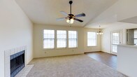 This single-floor residence offers a welcoming and well-lit interior designed for comfortable living. The main living area is generously proportioned, featuring soft carpeted flooring that transitions seamlessly into hardwood in the adjoining dining or flex space. A vaulted ceiling adds a sense of openness and grandeur to the room, enhanced by a ceiling fan with an integrated light fixture — ideal for year-round comfort. Multiple large windows line the walls, flooding the space with abundant natural light and creating a bright, airy atmosphere throughout the day. The adjacent area is complemented by an elegant chandelier, adding a refined touch to the open-plan layout. The light, neutral wall tones throughout contribute to a clean and versatile aesthetic, making the space easy to personalize. The textured ceiling adds a subtle architectural detail consistent across the interior. Overall, this home presents a spacious, functional, and inviting single-level layout that balances practicality with understated style, suited to a variety of living arrangements.