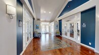 Located at 3700 Hermitage Dr in Voorhees, NJ, this single-story community clubhouse offers a generously proportioned, multi-functional facility designed for both relaxation and recreation. The grand entrance lobby immediately sets the tone with rich hardwood flooring, soaring vaulted ceilings, bold navy blue accent walls, and white French doors that flood the space with natural light. Tasteful framed artwork and comfortable seating areas flank the corridor, creating a warm and welcoming arrival experience.

The lounge area serves as a central gathering space, featuring the same warm hardwood floors, elevated ceilings, and a striking floor-to-ceiling stacked stone fireplace with a mounted flat-screen television. Large windows dressed with navy drapery allow abundant natural light to pour in, while classic upholstered seating and a glass-top coffee table complete the inviting atmosphere.

Adjacent to the lounge, the game room provides ample open space centered around a full-size billiard table beneath a stylish pendant light fixture. French doors and large windows offer views to the outdoors, enhancing the bright and airy feel.

The expansive fitness center is equipped with a comprehensive selection of cardio and strength-training equipment, including treadmills, ellipticals, and cable machines. Mirrored walls, recessed lighting, a wall-mounted television, and multiple windows ensure a bright, motivating workout environment throughout the day.
