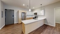 This single-story residence features a contemporary open-concept layout with wood-look plank flooring running throughout the entire unit. The kitchen serves as a central highlight, equipped with a spacious island featuring a built-in sink, sleek white countertops, and dual pendant lights overhead. Cabinetry combines light natural wood lower cabinets with crisp white upper cabinets, complemented by a full suite of stainless steel appliances including a refrigerator, electric range, microwave, and dishwasher. Recessed lighting illuminates the kitchen and adjoining living area, which includes a sliding glass door providing natural light and outdoor access.

The bedrooms are well-proportioned, each featuring wood-look flooring, neutral gray walls, and ceiling fans. At least one bedroom connects directly to a walk-in closet. The bathroom is cleanly finished with a stand-up shower, light wood vanity, white countertop, and open built-in shelving for storage. A dedicated laundry closet with louvered doors houses a full-size washer and dryer. Throughout the unit, neutral tones, clean lines, and consistent finishes create a cohesive, modern aesthetic.