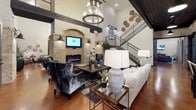 This clubhouse is a thoughtfully designed community gathering space that blends rustic Western character with modern comfort. The main lounge area commands attention with soaring ceilings, heavy exposed wood beams, and a dramatic floor-to-ceiling stone fireplace framed by brick accents and flanked by leather sofas and cowhide chairs. A grand chandelier anchors the space, while polished concrete floors run throughout, lending warmth and continuity.

Multiple seating zones offer versatile social settings. A media lounge features plush sectional sofas, a large wall-mounted television, and tufted leather banquette booths paired with marble-top tables and industrial-style pendant lighting. Equestrian-themed artwork adds a distinctive regional character across these areas.

The full kitchen is equipped with a generous island featuring quartz countertops, bar seating, pendant lighting, and a dark wood ceiling, with direct access to an outdoor area through glass-panel French doors. Additional nooks throughout the space offer intimate seating with curated décor, including large-scale canyon photography and sculptural wall art.

The entry area showcases soaring double-height ceilings, bold artwork, and access to multiple wings of the clubhouse. French doors along several walls invite natural light and provide views of the surrounding outdoor amenity areas, creating a bright and welcoming atmosphere throughout.