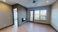 Located at 1100 E Third St in Fort Worth, TX, this contemporary single-floor residence offers a well-designed layout with modern finishes throughout. The open living area is a standout, anchored by a sleek built-in fireplace set against a bold dark accent wall. A ceiling fan overhead and large windows with city skyline views flood the space with natural light, while a glass door provides direct access to a private balcony overlooking the Fort Worth skyline. Light wood flooring runs consistently throughout the unit, tying the spaces together with warmth and continuity. The kitchen is thoughtfully appointed with crisp white cabinetry extending to the ceiling, a blue-green subway tile backsplash, white quartz countertops, and a full suite of stainless steel appliances including a French door refrigerator, electric range, microwave, and dishwasher. The bedrooms are generously sized with large windows that invite natural light and frame views of the surrounding cityscape. The bathroom features a dual-sink vanity with white countertops, modern hardware, wood-look tile flooring, and a well-lit mirror spanning the length of the vanity. Recessed lighting, neutral gray walls, and clean architectural lines contribute to the overall modern, urban ambiance of this Fort Worth residence.