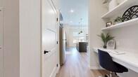 This thoughtfully designed single-floor residence offers a cohesive modern aesthetic throughout its efficiently arranged layout. The open-concept kitchen and dining area serves as a functional centerpiece, featuring two-tone cabinetry with dark lower cabinets and white upper cabinets, a white subway tile backsplash, light quartz countertops, and a full suite of stainless steel appliances including a refrigerator, range, microwave, and dishwasher. A dark pendant light anchors the space above the kitchen island, adding a striking contrast. Light-toned hardwood flooring flows seamlessly through the main living areas, enhancing the sense of openness. The living room benefits from multiple large windows that invite generous natural light, creating a warm and inviting ambiance. The bedroom is a comfortable retreat finished with plush carpet, tall ceilings, a large window, and direct access to a dedicated walk-in closet with built-in shelving. The bathroom is elegantly appointed with dark wood cabinetry, a white countertop vanity, black hardware accents, and a full tub-shower combination. A hallway connecting the main living spaces provides additional functionality, completing this well-appointed and stylish home.