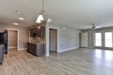 Located at Reservoir Dr in Canton, GA, this single-floor residence offers a well-designed layout with a clean, modern aesthetic. Light-toned hardwood-style flooring flows consistently throughout the space, complemented by neutral gray walls and crisp white baseboards and trim with elegant crown molding accents in the hallway.

The open living area is bright and generously proportioned, featuring a ceiling fan, large windows dressed with blinds, and glass French doors that lead to an outdoor balcony, allowing natural light to fill the room. Adjacent to the living space, a dedicated dining area is highlighted by a classic multi-arm chandelier, creating an inviting atmosphere for meals.

The galley-style kitchen is well-equipped, featuring rich dark cabinetry with modern hardware, granite-style countertops, a tile backsplash, a deep double-basin sink, and black appliances including a range and refrigerator. A walk-in pantry with built-in shelving provides ample storage.

The hallway connects the living areas to the private rooms via interior doors, maintaining a tidy flow throughout. The bathroom is a standout feature, offering a soaking tub with full tile surround, dark cabinetry with a granite-topped vanity, and wood-look flooring. A bedroom with carpet flooring adds warmth and comfort to the private quarters of the home.