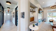 Located at 1800 Slaughter Rd in Huntsville, Alabama, this thoughtfully designed community clubhouse spans a generous single floor, offering a diverse range of amenities for residents. The welcoming entrance foyer greets visitors with light wood-look flooring, a statement ring chandelier, French doors flooding the space with natural light, and curated artwork that sets an inviting tone throughout.

The lounge area serves as the heart of the clubhouse, featuring a linear fireplace flanked by built-in shiplap shelving niches, comfortable seating in rich jewel tones, and a dramatic chandelier overhead. Large sliding glass doors provide views and access to an outdoor area. Adjacent to the lounge is a glass-enclosed conference room outfitted with a wooden table, upholstered chairs, and pendant lighting — ideal for meetings or collaborative work.

Private study nooks with built-in desks, wall sconces, and large windows overlooking lush green grounds offer quiet, focused workspaces. A café-style refreshment station features sage green cabinetry, a white countertop, and stylish décor accents.

The fitness center is well-equipped with cardio machines, strength equipment, floor-to-ceiling mirrors, large ceiling fans, and a distinctive checkered tile floor — with windows offering views of the pool area. Throughout, the design blends modern farmhouse aesthetics with contemporary finishes, creating a polished and functional community gathering space.