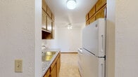 Located in Lauderdale, Minnesota, this two-bedroom, one-bathroom unit offers a straightforward single-floor layout designed for comfortable everyday living. The living room is the largest area in the home, featuring plush carpeting, a baseboard heating system, and a sliding glass door that allows natural light to fill the space. A wall-mounted air conditioning unit provides climate control. The room connects seamlessly to a hallway leading to the rest of the unit. The kitchen is equipped with warm wood cabinetry, a double-basin sink with light granite-style countertops, a white electric coil range, and tile flooring — offering a functional and efficient cooking space. Both bedrooms are carpeted and feature ceiling fans, baseboard heating, and windows with blinds that invite natural light and outdoor views. The primary bedroom includes a dedicated closet for storage. The full bathroom is finished with white tile walls and mosaic tile flooring, and includes a pedestal sink, toilet, a tub-shower combination, and an over-toilet storage cabinet with a mirrored medicine cabinet above the sink. Warm wood trim and doors are consistent throughout the unit, lending a cohesive and classic aesthetic to the overall space.