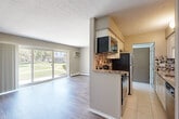 Located at 31200 Morlock St in Livonia, Michigan, this two-bedroom, one-bathroom unit offers a well-organized single-floor layout with a practical and comfortable living experience. The galley-style kitchen is a standout feature, showcasing white cabinetry, granite-look countertops, a decorative mosaic tile backsplash, stainless steel appliances, and light ceramic tile flooring. It opens conveniently toward the entrance and connects to the main living areas. The combined living and dining area is generously proportioned, featuring warm hardwood-style plank flooring, a ceiling fan, and a large sliding glass door that fills the space with natural light and provides direct access to the balcony, offering pleasant outdoor views of the surrounding green landscaping. Both bedrooms are carpeted and feature neutral tones, windows with views to the outdoors, baseboard heating, and wall-mounted air conditioning units. The primary bedroom is a comfortable size with ample room for furnishings. The bathroom is clean and bright, with white cabinetry, a tub-shower combo with tile surround, and wood-look flooring. Four closets throughout the unit provide generous storage. Textured ceilings and neutral wall tones carry throughout, lending a cohesive and move-in-ready feel to the entire space.