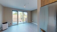 Located at 1280 Nehalem St in Portland, Oregon, this single-floor unit offers a thoughtfully designed layout with modern finishes throughout. The living area features light wood-tone flooring and neutral taupe walls, creating a calm and contemporary atmosphere. Large sliding glass doors open directly onto a private balcony, filling the space with abundant natural light and offering pleasant views of the surrounding Portland neighborhood and mature trees.

The galley-style kitchen is well-appointed with warm wood-grain cabinetry extending to the ceiling for ample storage, white quartz countertops, a subway tile backsplash, and a full suite of stainless steel appliances including a gas range, built-in microwave, dishwasher, and refrigerator. The kitchen connects seamlessly to the main living and sleeping areas, supporting an open and functional flow.

The sleeping area provides generous room for furnishings and includes a double sliding-door closet for organized storage. The bathroom is finished with a light quartz vanity countertop, wood-toned cabinetry, a large wall mirror, and a full tub-shower combination. Clean white walls and consistent flooring throughout the unit contribute to a cohesive, move-in-ready aesthetic suited to modern urban living in Southeast Portland.