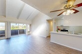 This single-floor residence offers a well-organized layout across two bedrooms and two bathrooms. The living room serves as the architectural centerpiece, distinguished by vaulted ceilings with exposed white-painted wood beams and a ceiling fan overhead. Light-toned hardwood flooring extends throughout the main living area, contributing to a clean, airy aesthetic. A wall of sliding glass doors opens directly onto a private balcony, providing generous natural light and outdoor views of surrounding greenery.

The kitchen is positioned adjacent to the living area in an open-concept arrangement, featuring a peninsula with a dual-basin sink and light quartz countertops, white cabinetry, and a gas range beneath an overhead ventilation hood. The layout promotes easy interaction between the cooking and living spaces.

The primary bedroom features tall ceilings with a clerestory window, hardwood flooring, and ample wall space. The second bedroom is carpeted, with a mirrored sliding-door closet and a large window offering outdoor views. Each bathroom is functionally appointed; one includes a tub-shower combination, single vanity, and hardwood flooring, while the other features an extended vanity with mirrored closet doors nearby.