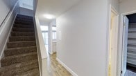 This two-story residence features 2 bedrooms and 2 bathrooms, offering a well-proportioned layout across two levels. The interior showcases clean, modern finishes, including smooth white walls, crisp white baseboards, and light wood-style flooring that extends through the main living areas, creating a bright and cohesive aesthetic. A carpeted staircase connects the two floors, providing a comfortable transition between the levels. The entryway is welcoming and functional, offering clear sightlines into the living areas and access to the staircase. Natural light filters into the space through windows visible toward the front of the home, contributing to an airy and open atmosphere. The kitchen features white cabinetry, maintaining the home's consistent, clean design language. The overall layout is practical and efficient, making good use of the available square footage across both floors. The neutral color palette and consistent use of materials throughout the home create a harmonious living environment that is both visually appealing and easy to personalize. This two-story home is well-suited for those seeking a comfortable, move-in-ready space with a modern sensibility.