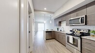 This well-appointed one-bedroom, one-bathroom unit offers a thoughtfully designed single-floor layout with a clean, contemporary aesthetic throughout. The open-concept living area features light-toned hardwood-style flooring and large sliding glass doors fitted with vertical blinds, allowing natural light to fill the space and providing access to an outdoor area.

The kitchen is a standout feature, equipped with a full suite of stainless steel appliances including a refrigerator, range, built-in microwave, and dishwasher. Flat-panel cabinetry in a warm taupe wood finish extends from floor to ceiling, complemented by granite countertops and a classic white subway tile backsplash. Pendant lighting adds a refined touch above the counter.

The bedroom is carpeted for comfort, offering a generous footprint with natural light from a window. It connects directly to a well-designed walk-in closet outfitted with built-in shelving, dual hanging rods, and integrated drawers, maximizing storage efficiency.

The bathroom features granite countertops atop a wood-toned vanity, dual framed mirrors, tile flooring, and a clean, neutral palette that reinforces the unit's modern, cohesive design.