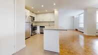 Located at 5 Brookbanks Dr in Toronto's M3A neighbourhood, this two-bedroom, one-bathroom unit offers a well-organized layout across a single floor. The open-concept kitchen and living area serves as the heart of the home, where a peninsula with a stone-edged countertop provides a natural divide between the two spaces. The kitchen is well-appointed with white shaker-style cabinetry, stainless steel appliances including a refrigerator, stove, microwave, and dishwasher, along with recessed pot lighting that creates a bright and functional workspace. The spacious living room is filled with natural light from large floor-to-ceiling windows and features warm parquet hardwood flooring that extends throughout the unit, adding a classic character to the space. Both bedrooms are generously sized, with the primary bedroom offering ample room and good natural light. The full bathroom includes a white vanity with storage, a toilet, and a soaker tub with white tile surround, finished in neutral tones throughout. A hallway connects the main living areas to the bedrooms and bathroom, providing a practical flow. The clean, bright palette of white walls and warm wood floors gives the entire unit a fresh, versatile feel.