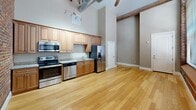 This 420 square foot loft-style apartment in Lawrence, MA, seamlessly blends historic charm with modern convenience. The space is characterized by its exposed brick walls, soaring ceilings, and large arched windows that flood the interior with natural light. The open floor plan maximizes the living area, featuring gleaming hardwood floors throughout.

The kitchen is a highlight, boasting light wood cabinetry, granite countertops, and stainless steel appliances including a full-size refrigerator, oven, and microwave. Track lighting and exposed ductwork add to the industrial-chic aesthetic.

A separate laundry area includes stacked washer and dryer units, enhancing the apartment's functionality. The bathroom, while not pictured, is mentioned in the property details.

The apartment's single floor layout and efficient use of space make it an ideal urban dwelling, offering a perfect balance of historical architecture and modern living in a prime location on Canal Street.