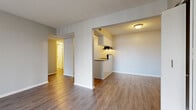 Located at 203 Burningtree Cir in Independence, MO, this single-floor, one-bedroom, one-bathroom residence offers a practical and functional layout. The living room is bright and airy, featuring wood-style vinyl flooring and a sliding glass door fitted with vertical blinds that allows ample natural light to flow into the space. The kitchen is semi-open to the living area, separated by a half-wall peninsula with a granite-style countertop that provides additional prep space. White cabinetry lines the kitchen walls, complemented by black appliances including a refrigerator and electric range, along with an under-cabinet range hood and a stainless steel sink. A hallway connects the main living area to the bedroom and bathroom. The spacious bedroom is carpeted for comfort and includes a closet, a window with blinds for natural light, and neutral-toned walls. The bathroom features a white vanity with a granite-style countertop, a mirror cabinet, tile-surround bathtub, and wood-style flooring that carries through from the rest of the unit. The entry foyer includes a closet for additional storage. Neutral gray tones, textured ceilings, and consistent finishes throughout lend the space a clean, cohesive appearance.