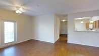 This single-floor residence offers a clean, functional layout designed for comfortable everyday living. The main living area is characterized by rich, warm-toned hardwood flooring that extends throughout the space, providing a cohesive and inviting atmosphere. Smooth white walls and a standard ceiling height contribute to a bright, open feel, while recessed and flush-mount lighting ensures the interior remains well-illuminated.

A central hallway connects the living area to additional rooms, including what appears to be a bathroom and entryway, visible at the far end of the corridor. The hallway's paneled door and soft ceiling light enhance the sense of a thoughtfully organized floor plan. To one side of the living space, an open pass-through or nook hints at an adjacent kitchen or utility area, maintaining a sense of flow and accessibility throughout the home.

The overall ambiance is understated and neutral, with a palette of whites and warm wood tones that creates a versatile backdrop well-suited for a variety of interior styles. The absence of clutter and the open sight lines between rooms make the space feel airy and easy to navigate. Clean baseboards and well-maintained walls reflect a tidy, move-in ready condition throughout this single-level home.