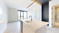 Located at 1111 Fairfield Avenue in Cleveland's 44113 zip code, this modern one-bedroom, one-bathroom unit showcases a clean, contemporary design with high-end finishes throughout its efficiently laid-out single floor. Light wood-tone flooring runs continuously across the open living and kitchen areas, enhancing the bright, airy atmosphere created by large, floor-to-ceiling windows that frame outdoor views of the surrounding neighborhood.

The open-concept kitchen is a standout feature, equipped with a central island topped with a white quartz countertop and a matte black gooseneck faucet. Contrasting dark cabinetry lines the kitchen walls, complemented by stainless steel appliances—including a refrigerator and range—and a textured subway tile backsplash. A sleek linear pendant light with warm gold accents anchors the kitchen-to-living transition.

The living area flows naturally from the kitchen, bathed in natural light from oversized windows. The bedroom is a well-proportioned, serene retreat with its own large window and the same continuous light wood flooring.

The bathroom offers a refined, spa-like feel with large-format tile flooring, a glass-enclosed walk-in shower with vertical subway tile, matte black fixtures, and a stacked washer/dryer unit for added convenience. A dedicated closet completes this well-appointed, move-in-ready space.