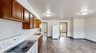 Located at 2109 College St in Cedar Falls, Iowa, this single-floor unit offers four bedrooms and one bathroom within a practical, well-organized layout. The kitchen serves as a central hub of the home, outfitted with warm oak cabinetry, light countertops, a double-basin sink, and white appliances including an electric range, dishwasher, and refrigerator. Durable wood-look flooring runs throughout the kitchen and living area, lending a cohesive feel to the shared space. The living room benefits from natural light through windows fitted with wood-trimmed blinds. Each of the four bedrooms features neutral walls and carpeted floors, with some rooms offering closet storage. The primary bedroom includes a closet and direct sightlines to the kitchen, enhancing the unit's functional flow. Additional bedrooms are comfortably proportioned with carpet flooring and access to natural light. The single bathroom is equipped with a standalone walk-in shower with a clean, tiled surround. Throughout the unit, warm wood door and window trim provides a consistent design accent, complementing the neutral color palette and making the space feel inviting and move-in ready.