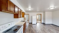 Located at 2109 College St in Cedar Falls, Iowa, this single-floor unit offers four bedrooms and one bathroom within a practical, well-organized layout. The kitchen serves as a central hub of the home, outfitted with warm oak cabinetry, light countertops, a double-basin sink, and white appliances including an electric range, dishwasher, and refrigerator. Durable wood-look flooring runs throughout the kitchen and living area, lending a cohesive feel to the shared space. The living room benefits from natural light through windows fitted with wood-trimmed blinds. Each of the four bedrooms features neutral walls and carpeted floors, with some rooms offering closet storage. The primary bedroom includes a closet and direct sightlines to the kitchen, enhancing the unit's functional flow. Additional bedrooms are comfortably proportioned with carpet flooring and access to natural light. The single bathroom is equipped with a standalone walk-in shower with a clean, tiled surround. Throughout the unit, warm wood door and window trim provides a consistent design accent, complementing the neutral color palette and making the space feel inviting and move-in ready.