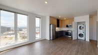 Located on an upper floor at 15 N Grant St in Spokane, Washington, this modern unit offers a bright, open-concept layout designed with clean lines and a contemporary aesthetic throughout. Wide-plank hardwood-style flooring runs seamlessly across the living areas, complementing the crisp white walls and smooth ceilings.

The open living area is anchored by a striking bank of tall, floor-to-ceiling windows that flood the space with natural light and frame expansive views of the Spokane cityscape and surrounding mountains. The kitchen is thoughtfully appointed with two-tone cabinetry—warm wood uppers paired with slate-gray lower cabinets—stainless steel appliances including a refrigerator, range, and microwave, a clean white countertop, and a single-basin sink.

The bedroom features sliding closet doors and a wall-mounted mini-split HVAC unit, ensuring year-round climate control. The bathroom is finished with durable wood-tone flooring, a dark-base vanity with a white countertop, and brushed nickel fixtures. A dedicated in-unit laundry closet with a stacked washer and dryer adds everyday convenience. The overall ambiance is clean, minimal, and move-in ready, reflecting a modern urban lifestyle in the heart of Spokane.