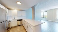 Located at 170 Washington St in Haverhill, MA, this well-appointed one-bedroom, one-bathroom residence offers a thoughtfully designed layout across a single floor. The open-concept kitchen and living area serves as the heart of the home, featuring white shaker cabinetry with gold-tone hardware, light quartz countertops, and a full suite of stainless steel appliances including a range, microwave, and dishwasher. A peninsula with bar seating provides additional workspace and a natural division between the kitchen and living area. An exposed structural column adds an architectural character reminiscent of industrial-style loft design. The living area is finished with light hardwood-style flooring and large windows that invite abundant natural light and offer elevated views of the surrounding Haverhill landscape. The spacious bedroom features plush wall-to-wall carpeting, soft neutral tones, and a dedicated closet with built-in shelving. The full bathroom is finished with a white vanity, quartz countertop, and a tub/shower combination. A neutral color palette throughout the residence creates a clean, modern aesthetic, while the light-toned flooring and large windows contribute to an airy, bright ambiance throughout the home.