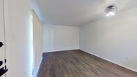 This single-story residence presents a well-maintained, move-in-ready interior defined by a consistent neutral color palette and dark hardwood-style flooring that runs throughout the main living areas. The living space is open and simply designed, with crisp white walls, clean baseboards, and a ceiling-mounted light fixture that adds a contemporary touch. Vertical blinds along a large window allow for adjustable natural light while maintaining privacy. The front entry connects seamlessly to the living area, which also features a ceiling fan in the adjoining room for added comfort.

The galley-style kitchen is efficiently laid out with white cabinetry, white countertops, and a classic subway tile backsplash. Stainless steel appliances — including a refrigerator, electric range, microwave, and dishwasher — provide a modern, functional cooking environment. The dark hardwood-style flooring continues into the kitchen, maintaining visual cohesion throughout.

The bedroom features plush carpeting for comfort and connects directly to a bathroom area equipped with a vanity featuring a white countertop, dark hardware, and an adjacent tub/shower combination. The overall ambiance of the space is clean, understated, and functional.