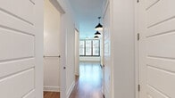 Located at 601 Indian St in Savannah, Georgia, this efficiently designed single-floor unit offers a thoughtful layout that maximizes every square foot. The interior is finished with warm hardwood-style flooring throughout, crisp white walls, and clean modern trim that create a bright, cohesive aesthetic.

A central hallway connects the space, lined with pendant lighting that adds a contemporary touch. The main living area is bathed in natural light through large, floor-to-ceiling windows fitted with blinds, offering views of the surrounding Savannah streetscape. A ceiling fan adds comfort to this open, airy room.

The kitchen is well-appointed with white shaker cabinetry extending to the ceiling for ample storage, a herringbone tile backsplash, light stone countertops, and stainless steel appliances including a side-by-side refrigerator with water dispenser, electric range, and over-the-range microwave.

The bathroom features a white vanity with a marble-style countertop, a framed mirror, stylish linear vanity lighting, and a tiled shower-tub combination. Additional conveniences include a dedicated closet with wire shelving, a laundry area, and a utility room. The unit's clean, modern finishes and functional layout make it a well-organized and comfortable Savannah residence.