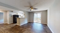 Located at 1700 Hunter Ridge Lane in Peachtree Corners, Georgia, this one-bedroom, one-bathroom residence offers a well-designed single-floor layout that maximizes both functionality and comfort. The open-concept living and dining area is anchored by rich, dark hardwood-style flooring and neutral gray walls, creating a clean and contemporary aesthetic throughout. A ceiling fan with integrated lighting provides both airflow and illumination, while a sliding glass door floods the space with natural light and opens directly onto a private balcony with outdoor views. The kitchen is positioned adjacent to the living area and features white cabinetry, a stone-look countertop with a breakfast bar peninsula, a black refrigerator, and a window above the sink that brings in additional natural light. The bedroom is generously proportioned, finished with plush carpeting, a ceiling fan, and a window that allows for natural ventilation and light. Multiple closet access points provide ample storage. The bathroom includes a full tub-shower combination with a rainfall showerhead, clean white surround panels, and brushed nickel fixtures. Textured ceilings are consistent throughout the unit, adding a classic touch. The overall ambiance is bright, functional, and move-in ready.