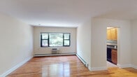 Located at 290 North Broadway in Hicksville, NY, Eagle Rock Hicksville presents a thoughtfully laid-out single-floor residence that balances comfort and functionality. Throughout the unit, warm-toned hardwood flooring adds a sense of continuity and character, complementing the clean, neutral-painted walls.

The spacious living area is a standout feature, bathed in natural light through large windows that offer pleasant views of surrounding greenery. Baseboard heating and a wall-mounted air conditioning unit ensure year-round climate control. The open feel of the living space is enhanced by its generous proportions and smooth white ceilings.

Positioned just off the main living area, the kitchen is accessible through a dedicated doorway and is equipped with wooden cabinetry, a countertop workspace, and essential appliances, providing an efficient and organized cooking environment.

The bedroom is a quiet, well-sized room with its own window framing outdoor foliage, continuing the hardwood flooring and neutral palette found throughout the unit.

The bathroom is elegantly finished with large-format beige tiles, a decorative mosaic accent border in warm earth tones, a tub-shower combination, and a dark granite vanity with an undermount sink — adding a refined touch to the overall interior.

A private entry door completes this well-appointed residence, ideally situated in the heart of Hicksville.