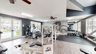 Located at 5332 Bleecker St in Virginia Beach, VA, this fitness center is a thoughtfully designed single-floor facility that balances function and aesthetic appeal. The space features a neutral color palette of slate gray walls paired with light wood-style flooring, creating a clean and modern atmosphere conducive to focused workouts.

The facility is outfitted with a comprehensive selection of equipment, including treadmills, elliptical trainers, a rowing machine, stationary bikes, and a Cybex multi-station strength machine, alongside a cable machine and free weight rack stocked with dumbbells and medicine balls. A dedicated stretching and floor exercise area features rubber matting, providing a practical space for warm-ups or flexibility work.

A standout design feature is a large brick-texture accent wall adorned with a bold cyclist mural and the motivational phrase "Break Your Limits," adding an energetic, urban edge to the interior. Full-length mirrors are positioned along one wall to support proper form during exercise.

Natural light is a defining characteristic of the space, with multiple large windows overlooking the surrounding landscaping and community grounds. Vaulted ceilings with clerestory windows in one section further enhance the sense of openness and airiness. Ceiling fans provide additional air circulation throughout. The overall ambiance is bright, motivating, and well-maintained.
