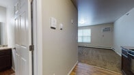 This single-floor unit offers a straightforward, functional layout designed for comfortable everyday living. The entry corridor features warm wood-style flooring and neutral gray walls, with a thermostat and security panel conveniently mounted near the entrance. A wall-unit air conditioner and baseboard heating are present throughout, ensuring year-round climate control.

The kitchen is efficiently arranged with rich dark espresso cabinetry extending to the ceiling, granite-style laminate countertops, and a full suite of black appliances including a range, microwave, dishwasher, and refrigerator. Wood-style flooring continues seamlessly through this space, transitioning into the adjacent areas.

The bedroom is a generously sized room with plush neutral carpet, a large window fitted with blinds for natural light and privacy, baseboard heating, and a six-panel door. The open feel of the room provides ample space for furnishings.

The bathroom features the same wood-style flooring found at the entry, a dark espresso vanity with a granite-style countertop, a large mirror with overhead lighting, and clean white fixtures. The layout is open and well-lit.

The living area is spacious with soft carpet, neutral walls, a window unit, and baseboard heating, offering a versatile and welcoming space throughout.