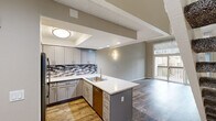 Located at 2800 Madison Ave in Fullerton, California, this two-story residence offers a well-organized layout with contemporary finishes throughout. The main level centers on an open-concept kitchen and living area, where the kitchen stands out as a functional and stylish focal point. It features gray shaker-style cabinetry, a mosaic tile backsplash in neutral tones, quartz countertops with a marble-like finish, and a peninsula with an integrated sink that extends into the living space. Stainless steel appliances, including a refrigerator, range, and microwave, complete the setup. Recessed lighting and wall sconces provide layered illumination, while a staircase with white balusters connects to the upper floor. Wood-look vinyl flooring runs throughout the main level, adding warmth and durability. A stacked washer and dryer unit is conveniently housed near a bathroom on the main floor. The upper level contains additional rooms with the same wood-look flooring, textured ceilings, and neutral walls, including spaces with windows offering natural light and tree-lined views. An enclosed outdoor patio with a wood lattice fence provides a private exterior retreat with views of mature pine trees.