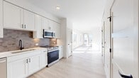 Located on S Santa Fe Dr in Sheridan, Colorado, this thoughtfully designed one-bedroom unit offers a clean, modern aesthetic across its single-floor layout. The interior is finished with light hardwood-style flooring throughout, crisp white walls, and panel-style doors with matte black hardware, creating a cohesive and contemporary atmosphere.

The kitchen is a standout feature, outfitted with white shaker-style cabinetry extending to the ceiling for ample storage, a gray subway tile backsplash, and a full suite of stainless steel appliances including a side-by-side refrigerator with ice maker, electric range, built-in microwave, and dishwasher. Light countertops and a single-basin sink complete the functional and stylish workspace.

The bedroom is a bright, comfortable retreat enhanced by a large window framing sweeping views of the surrounding landscape and distant mountains under open Colorado skies. Natural light floods the room, highlighting the clean finishes. A dedicated closet with built-in shelving and hanging rods provides well-organized storage.

The layout flows efficiently from the entry corridor past the kitchen and into the living area, where large windows draw in abundant natural light and outdoor views. The overall design prioritizes clean lines, neutral tones, and modern finishes, making this a well-appointed space in the Sheridan community.