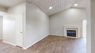 This single-story, 2-bedroom, 2-bathroom home offers a thoughtfully designed layout that balances comfort and functionality. The living room serves as the heart of the home, showcasing a striking vaulted ceiling clad in whitewashed shiplap planks that adds warmth and architectural character. A tile-surround fireplace with a clean white mantel anchors the space, while wood-look flooring flows throughout, complementing the neutral, light gray walls.

The kitchen is equipped with stainless steel appliances, including a refrigerator, range, and microwave, set against light wood cabinetry and a classic subway tile backsplash. A peninsula with a white quartz-style countertop provides additional prep space and casual seating opportunity.

Both bedrooms are carpeted and feature crown molding, ceiling fans, and ample natural light from large windows with blinds. The generously sized primary bedroom includes a walk-in closet outfitted with wire shelving for organized storage. The second bedroom also benefits from a dedicated closet and easy hallway access.

The bathrooms are finished with light wood vanities, quartz countertops, and walk-in glass-door showers. Wood-look tile flooring carries through the bathrooms, maintaining a cohesive aesthetic. Multiple hallways connect the spaces efficiently, completing this well-organized and move-in ready home.