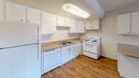 This single-floor unit offers a practical and comfortable layout designed for everyday living. The open-concept living and dining area features warm wood-style laminate flooring that extends throughout the main living spaces, creating a cohesive and inviting atmosphere. A large window with vertical blinds allows natural light to fill the room, enhancing its bright and airy feel. The kitchen is efficiently designed with white cabinetry, a laminate countertop, a double-basin sink, and white appliances including a refrigerator, dishwasher, and electric range. An overhead fluorescent light fixture provides ample task lighting. A peninsula counter connects the kitchen to the living area, offering additional prep space and a natural divide between the two zones. The bedroom is carpeted for comfort and features a textured ceiling, a window with an exterior view, and two separate doorways — one leading to a dedicated closet with a hanging rod and the other opening to the hallway. The bathroom includes a single-sink vanity with under-cabinet storage, a lighted mirror, wood-style flooring, and a classic white toilet. Throughout the unit, neutral tones and clean finishes create a functional, move-in-ready environment.