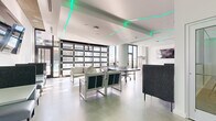This single-floor amenity space delivers a contemporary recreational experience defined by a striking combination of modern design and versatile leisure features. The open-plan layout is anchored by polished concrete floors that extend throughout, lending the space an industrial-chic aesthetic that complements the crisp white walls and exposed structural columns.

A defining architectural feature is the geometric teal LED strip lighting embedded into the ceiling, creating a dynamic, futuristic ambiance that energizes the entire space. Large floor-to-ceiling windows and glass-panel garage-style doors flood the interior with abundant natural light, while offering views of the surrounding outdoor area.

The space is thoughtfully zoned for multiple activities. A full-size pool table in light wood tones occupies a bright corner near the expansive windows, while a regulation ping pong table provides additional gaming options. Arcade machines add a playful element along one wall. Multiple lounge seating arrangements—featuring contemporary white and charcoal upholstered furniture—offer relaxed gathering areas throughout. A wall-mounted flat-screen television enhances the entertainment offerings. The overall atmosphere is sleek, social, and purpose-built for active recreation and casual communal use.