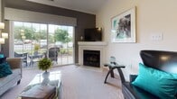 This single-floor residence offers a thoughtfully designed layout that balances comfort and functionality throughout. The living room serves as the heart of the home, anchored by a corner fireplace with a clean white mantel and complemented by plush carpeting, crown molding, and a sliding glass door that opens to a private patio, filling the space with natural light and outdoor views. Adjacent to the living area, a dedicated dining nook features a bold teal accent wall with chair rail detail, a built-in desk, and pendant lighting — ideal for both casual dining and working from home. The galley-style kitchen is outfitted with rich cherry cabinetry, granite-look countertops, black appliances, and durable hardwood-style flooring. A door off the kitchen leads directly to an in-unit laundry area, adding everyday convenience. The primary bedroom offers generous proportions, soft carpeting, a ceiling fan, a walk-in closet, and an en-suite bath. The second bedroom mirrors similar comforts with sage green walls, natural light from a window with exterior views, and its own closet and bathroom access. A full bathroom with a tub-shower combination, hardwood-style flooring, and a wood-toned vanity rounds out the space. Throughout, neutral tones and consistent finishes create a cohesive, welcoming ambiance.