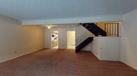Located at 1987 Mohawk Pl in Kent, Ohio, this two-story residence offers a practical and functional layout spread across two levels. The main floor features a generously sized living area with warm carpeting, a textured ceiling, and a ceiling fan. A bold black staircase with metal railings connects the floors and serves as a visual focal point. The living space flows into a dedicated kitchen equipped with wood-toned cabinetry, a double sink, white electric range, microwave, and light-toned flooring, with a window providing natural light. A half bathroom on this level includes a wood-vanity with a white countertop. The lower level presents an expansive open living space with sliding glass doors that invite natural light and views of the surrounding wooded scenery. Upstairs, the bedrooms feature plush carpeting, ceiling fans, and wall-mounted air conditioning units. A standout bedroom offers dual closets, providing excellent storage capacity. The full bathroom includes a tiled tub-shower combination and light tile flooring. Throughout the home, neutral tones and carpeted floors create a cohesive and understated ambiance suited for comfortable everyday living.