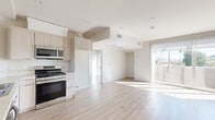 Located at 5501–5513 Laurel Canyon Blvd in Valley Village, Los Angeles, this modern 1-bedroom, 2-bathroom unit offers a thoughtfully designed open-concept layout filled with natural light. Light wood-tone flooring runs throughout, complementing the clean white walls and contemporary finishes that define the space.

The combined kitchen and living area serves as the heart of the unit. The kitchen is outfitted with light wood cabinetry, stone-look countertops, and a full suite of stainless steel appliances including a gas range, built-in microwave, and dishwasher. The open living area flows seamlessly toward a wall of sliding glass doors that open to one of two private balconies, offering views of palm tree-lined surroundings and bringing in abundant Southern California sunshine.

The bedroom is a well-proportioned retreat featuring its own sliding glass door access to a second balcony, a mirrored closet, and generous natural light. The unit includes two full bathrooms — one with a white vanity and classic fixtures, and a second featuring a glass-enclosed tiled shower. Additional conveniences include an in-unit laundry area and a dedicated closet. The overall ambiance is clean, bright, and move-in ready, reflecting a modern aesthetic suited to contemporary urban living.