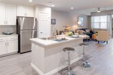 This well-appointed 1-bedroom, 1-bathroom residence at 3145 Market Street in Riverside, California offers a thoughtfully designed single-level open-concept layout. The kitchen is a standout feature, showcasing crisp white shaker cabinetry extending to the ceiling, quartz countertops, stainless steel appliances including a gas range, microwave, and refrigerator, and a central island with a double sink and bar seating — ideal for both cooking and casual dining. The kitchen flows seamlessly into the dining and living areas, which are finished with light wood-style flooring and recessed lighting throughout. The living room is bright and welcoming, with a ceiling fan, large windows dressed with blinds, and access to a private balcony that brings in natural light and outdoor views. The bedroom is a serene retreat, featuring multiple windows, ample natural light, and the same warm wood-style flooring. The full bathroom is cleanly finished with white cabinetry, a wide vanity mirror, a tub/shower combination, and direct access to a walk-in closet with built-in shelving. An in-unit laundry area adds everyday convenience, rounding out this modern and functional Riverside residence.