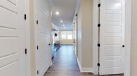 This single-floor space offers a thoughtfully designed layout with a cohesive aesthetic throughout. Wood-look tile flooring runs through the main living and kitchen areas, providing a warm and durable foundation that ties the space together visually.

The kitchen is well-equipped with rich, dark-stained wood cabinetry, granite-look countertops, and a full suite of stainless steel appliances including a range, over-the-range microwave, refrigerator, and dishwasher. Recessed lighting illuminates the workspace efficiently, and crown molding adds a refined finishing touch.

A wide hallway connects the kitchen to the main living area, flanked by white panel doors with black hardware accents. The hallway features built-in cabinetry, providing ample storage. The living area benefits from generous natural light through large windows fitted with dual-shade roller blinds, and a sliding glass door opens to an outdoor balcony or patio enclosed by decorative iron railings. The views extend across an open landscape, giving the space an airy, expansive feel.

The bathroom includes a vanity with granite-look countertops and dark wood cabinetry, wood-look tile flooring, and a combination tub and shower with stone-surround tile walls. A separate carpeted room with a wall-mounted mini-split HVAC unit rounds out the layout, offering a comfortable and climate-controlled space.
