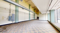 Located at 320 N Huron St in the heart of downtown Toledo, Ohio, this single-floor commercial green space offers a generously open and versatile layout spanning nearly three thousand square feet. The space features a notably open floor plan, making it well-suited for a variety of commercial or community uses. A hallmark of the interior is the classic checkered tile flooring that runs throughout, lending a retro character to the space. The high ceilings add a sense of volume and airiness, while exposed ductwork and industrial-style HVAC components contribute to a raw, functional aesthetic. Large storefront windows along the street-facing facade flood the interior with natural light and provide clear views of the surrounding downtown streetscape, creating a strong visual connection to the urban environment outside. Green-painted structural columns and accents punctuate the cream and yellow walls, adding architectural interest. A raised platform area near the windows adds dimensional variety to the floor plan. Restroom facilities are accessible from within the space, indicated by interior signage. The space is currently in shell condition, presenting an open canvas ideal for buildout tailored to a new tenant's or operator's vision. Its prominent downtown location and expansive, light-filled interior make it a compelling opportunity for retail, hospitality, or community-oriented use.