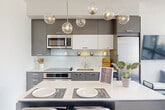Located in the heart of Washington, DC's vibrant Logan Circle neighborhood, this thoughtfully designed one-bedroom, one-bathroom residence offers a clean, contemporary aesthetic throughout. Light wood flooring flows seamlessly across the open-plan living, dining, and kitchen area, creating a cohesive and airy atmosphere. The modern kitchen is a standout, featuring flat-panel cabinetry in a warm linen finish, a crisp tile backsplash, stainless steel appliances including a built-in microwave, electric range, and dishwasher, and a generous white quartz island topped by a striking multi-globe brass pendant light. The living and dining space flows naturally from the kitchen, offering a versatile layout. A separate den provides additional flexible living space. The bedroom is a bright, calm retreat, benefiting from oversized windows that frame views of the surrounding DC streetscape, and is complemented by a large sliding-door closet. The bathroom is elegantly appointed with large-format tile, a floating wood vanity, and a glass-enclosed walk-in shower with a rainfall showerhead. Two closets throughout the residence provide practical storage. The unit's crisp white walls, recessed lighting, and minimalist finishes give it a polished, move-in-ready appeal.