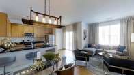Located at 417 Raritan Road in Roselle, New Jersey, this single-floor residence offers a thoughtfully designed open-concept layout that seamlessly connects the kitchen, dining, and living areas. The kitchen is equipped with stainless steel appliances, warm wood cabinetry, dark stone countertops, and a breakfast bar, all illuminated by a striking industrial-style pendant light fixture with Edison bulbs suspended from a wood and chain frame. The dining area flows naturally from the kitchen, centered around a glass-top table with contemporary seating. The living room is bright and welcoming, benefiting from generous natural light streaming through large windows dressed with patterned curtains. Sliding glass doors open to an outdoor area, enhancing the sense of openness and providing easy access to the exterior. Warm hardwood flooring runs throughout, tying the spaces together cohesively. The living area is styled with modern furniture, including a sectional sofa and accent chairs, layered over a textured area rug. The overall ambiance is modern yet comfortable, combining practical design with stylish details that make this a well-appointed and inviting home in the heart of Roselle, NJ.