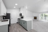 This single-floor residence offers a thoughtfully designed layout with a bright, neutral palette and a blend of carpet and wood-look flooring throughout. The spacious living room serves as a central gathering space, anchored by a framed fireplace and a large sliding glass door that opens to a private balcony, flooding the room with natural light and providing views of surrounding greenery.

Adjacent to the living area, the open-concept dining and kitchen space features a peninsula with bar-height seating, an elegant chandelier, and a decorative arched wall niche that adds architectural character. The kitchen is well-appointed with white upper cabinetry, sage green lower cabinets, white quartz countertops, a subway tile backsplash, stainless steel appliances including a refrigerator and dishwasher, and light wood-look flooring.

The bedrooms are carpeted and generously sized, each benefiting from windows with blinds that invite natural light. The full bathroom includes a white vanity with ample cabinet storage, a large mirror, patterned tile flooring, and a tub-shower combination. A second bathroom features wood-look tile flooring, a walk-in shower with frosted glass, and clean, minimalist finishes. Overall, the space presents a fresh, move-in ready aesthetic.