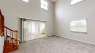 Located at 399 S Grant Ave in Columbus, Ohio, this two-story, 3-bedroom, 2-bathroom home offers a well-designed layout across two floors. The main level provides the majority of the living space, featuring an open-concept kitchen and living area. The kitchen is outfitted with crisp white shaker cabinets, granite-look countertops, a subway tile backsplash, black appliances, and light hardwood-style flooring that flows throughout the main level. The living area is immediately notable for its dramatically soaring ceilings, with tall windows positioned at multiple heights that flood the space with natural light. Sliding glass doors connect the living area to an enclosed sunroom-style porch featuring large panoramic windows and warm hardwood floors, offering views of the surrounding neighborhood. The bathrooms are finished with granite-top white vanities; one includes a tub/shower combo with tile flooring, while the other features a clean, compact layout. The bedrooms are carpeted and well-lit by natural light through blinded windows, offering a comfortable and quiet retreat. Two closets provide ample storage. The upper level houses additional bedrooms and benefits from the dramatic ceiling volume visible from below. Throughout, the home maintains a neutral, warm palette that lends a clean and move-in ready feel.