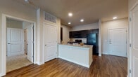 Located at 4835 Lord Rd in San Antonio, TX, this single-floor unit offers a thoughtfully designed open-concept layout. The kitchen serves as a central hub, showcasing dark espresso cabinetry, granite countertops, a peninsula island with an integrated sink, and black appliances including a refrigerator, range, and built-in microwave. Recessed lighting and track lighting illuminate the space throughout the main living and kitchen areas.

Rich wood-style flooring runs throughout the main living spaces, complementing the neutral warm-toned walls and crisp white trim. The living area is generously sized, featuring a ceiling fan and access to a private balcony through a glass door, allowing natural light to fill the room with outdoor views. A set of double doors opens to additional storage or utility space.

The bedrooms are carpeted for comfort, with large windows fitted with blinds that invite natural light while maintaining privacy. One bedroom features a ceiling fan and direct access to the balcony. The bathrooms are finished with dark vanity cabinetry, white countertops, large mirrors, and wood-style flooring, maintaining a consistent design aesthetic throughout. A walk-in closet is accessible from one of the bathrooms, adding practical storage to the overall floor plan.