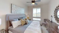 This well-designed single-floor residence combines contemporary style with functional living. The living area makes a strong architectural statement with its exposed industrial ductwork running along bright white ceilings, rich hardwood flooring, and a ceiling fan overhead. Large windows flood the space with natural light and frame views of lush greenery and surrounding buildings. The open layout connects seamlessly to a fully equipped kitchen, which features warm wood cabinetry, granite countertops, a classic tile backsplash, and a full suite of stainless steel appliances including a gas range, microwave, and French door refrigerator. The bedroom is a comfortable retreat, carpeted for warmth, with a ceiling fan, generous windows offering outdoor views, and ample space for a full bedroom suite. The primary bathroom is notably spacious, featuring a long dual-sink vanity with rich wood cabinetry, a glass-enclosed shower, a soaking tub, and recessed lighting throughout. A second bathroom mirrors the refined aesthetic with a single vanity, tile flooring, and a large mirror. A private balcony rounds out the space, overlooking a verdant landscaped courtyard with mature trees and walkways.