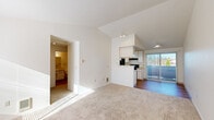 Located at 15655 SW Blanton St in Beaverton, Oregon, this 2-bedroom, 1-bathroom residence offers a thoughtfully laid-out single-level floor plan. The living area is anchored by vaulted ceilings that create an airy sense of height, with soft carpet underfoot and a sliding glass door that opens to a private balcony, allowing natural light to flow in and offering views of the surrounding greenery. A peninsula-style pass-through connects the living space to the galley kitchen, which features white cabinetry, light countertops, warm hardwood-style flooring, and black appliances including a refrigerator and electric range. Both bedrooms are carpeted and filled with natural light from their respective windows, each equipped with sliding mirrored closet doors for added storage. A walk-in closet with wire shelving provides additional organization space. The bathroom includes a full tub and shower combination with clean, white surround. A hallway connects the main living areas to the bedrooms and bathroom, creating a practical and efficient flow throughout. The entry area features hardwood-style flooring that transitions seamlessly into the carpeted living space, rounding out a clean and functional layout.