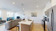 Located at 5232 Federal Blvd in Denver, CO, this well-designed two-bedroom, two-bathroom unit offers a efficient and modern single-floor layout. The open-concept kitchen and living area serves as the heart of the space, featuring light wood flooring that flows throughout. The kitchen is outfitted with stainless steel appliances, including a gas range, microwave, and refrigerator, complemented by white upper cabinetry, warm wood lower cabinets, and a central island with a white quartz countertop and integrated sink—ideal for both meal prep and casual dining with bar stool seating.

The living room receives abundant natural light through large sliding glass doors that open to a private balcony offering views of the surrounding neighborhood. The primary bedroom is a comfortable retreat, while the second bedroom features a window with scenic views toward open greenery and distant mountains. Both bathrooms are finished with modern fixtures; one includes a marble-tiled tub-shower combination, while the other features a floor-to-ceiling tiled walk-in shower with a mosaic hex-tile floor and built-in niche. Recessed lighting and a clean, neutral palette contribute to a bright, contemporary ambiance throughout.