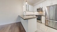 Located at 130 Raglan Ave in Toronto's vibrant Cedarvale neighbourhood, this one-bedroom, one-bathroom townhome offers a thoughtfully designed single-floor layout that maximizes every square foot. The interior is finished with rich hardwood flooring throughout the living areas, creating a warm and cohesive aesthetic.

The kitchen is a standout feature, showcasing crisp white cabinetry with glass-front upper cabinets, granite countertops, and a peninsula with an integrated sink — ideal for casual dining or meal prep. Stainless steel appliances, a subway tile backsplash, and stylish pendant lighting complete the modern look.

The bedroom is bright and airy, bathed in natural light from a large multi-pane window that frames lush green treetop views. A mirrored sliding-door closet adds both storage and a sense of depth to the room.

The bathroom features tile flooring and a soaker tub, with a convenient stacked washer and dryer tucked into an adjacent laundry closet — a practical touch that adds everyday ease.

A dedicated entrance welcomes residents into the space, rounding out a functional and stylish layout well-suited for those seeking comfortable urban living in one of Toronto's sought-after neighbourhoods.